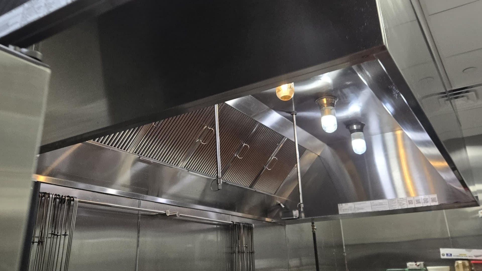 Looking up into a restaurant's existing exhaust hood: baffle filters and globe lights over the cook line